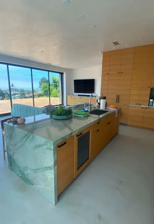 Modern kitchen with a green marble island, wood cabinets, and large windows with a view.