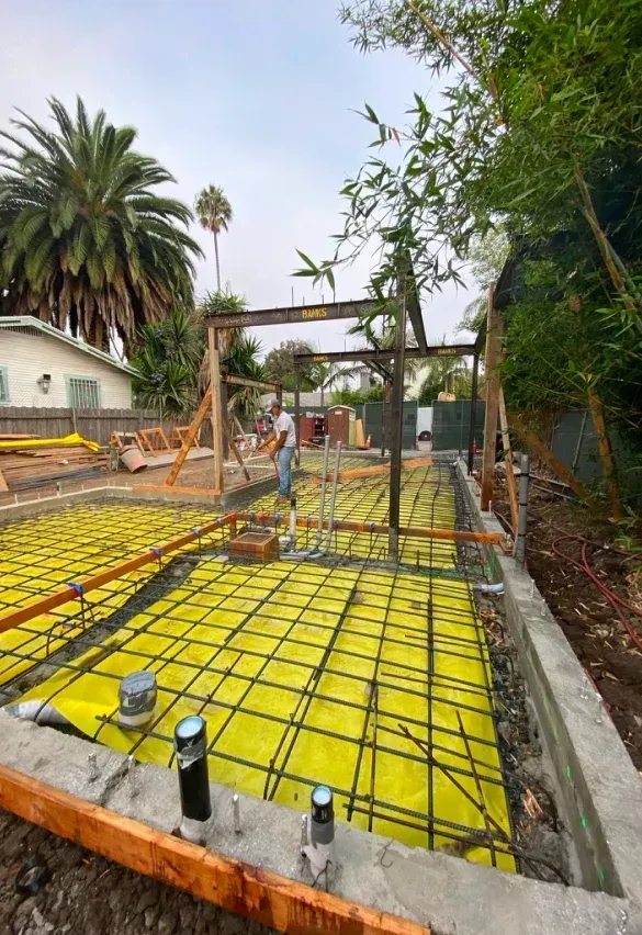 A concrete base is being built in a backyard with a palm tree in the background.
