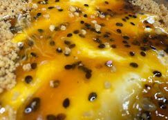 Primo piano di un dessert al frutto della passione con una vivace guarnizione di frutta gialla, semi neri e un bordo di crosta friabile.