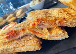 Una pila di pasta sfoglia dorata ripiena di formaggio fuso e salsa rossa su un vassoio nero.