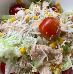 Primo piano di un'insalata di pollo con lattuga, pomodorini, mais e una generosa spolverata di formaggio grattugiato.