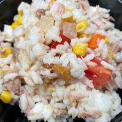 Primo piano di una ciotola di insalata di riso al tonno con mais, pomodori a cubetti e altre verdure.