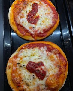 Due piccole pizze rotonde con salsa di pomodoro, formaggio fuso ed erbe aromatiche, disposte verticalmente su una teglia nera.