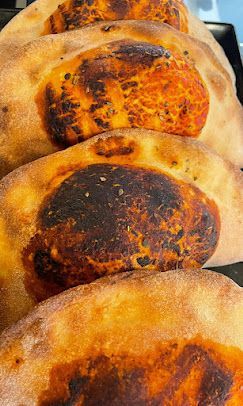 Una vista ravvicinata, dall'alto, di diversi calzoni cotti al forno, dorati e con il ripieno di salsa di pomodoro leggermente bruciacchiato, disposti in fila.