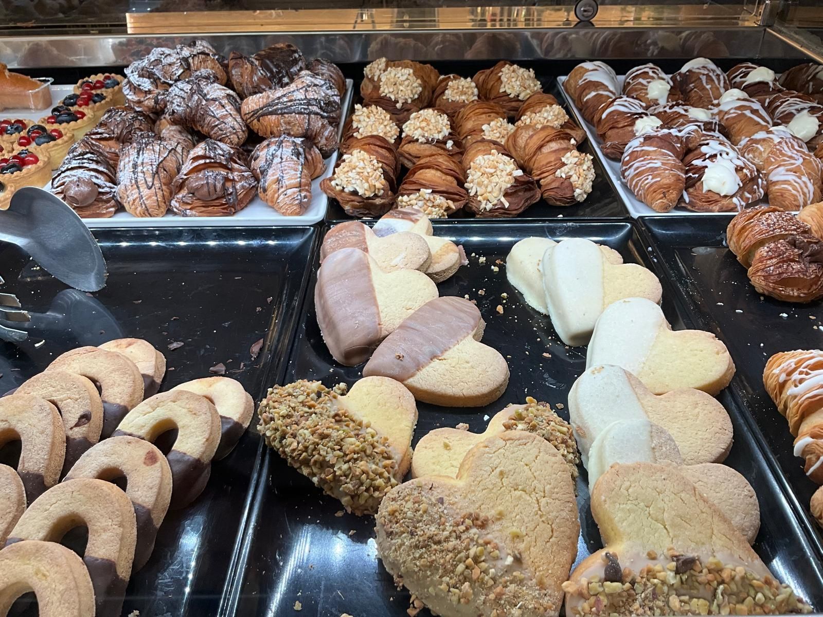 Una vetrina da pasticceria con file di vari dolci, tra cui croissant, biscotti decorati e biscotti a forma di cuore.