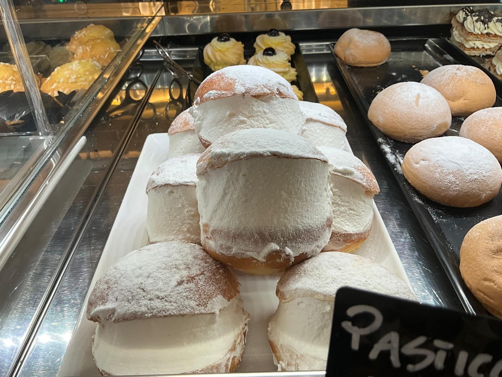 In una pasticceria, un vassoio bianco colmo di Maritozzo, soffici brioche traboccanti di panna montata e spolverate di zucchero a velo.
