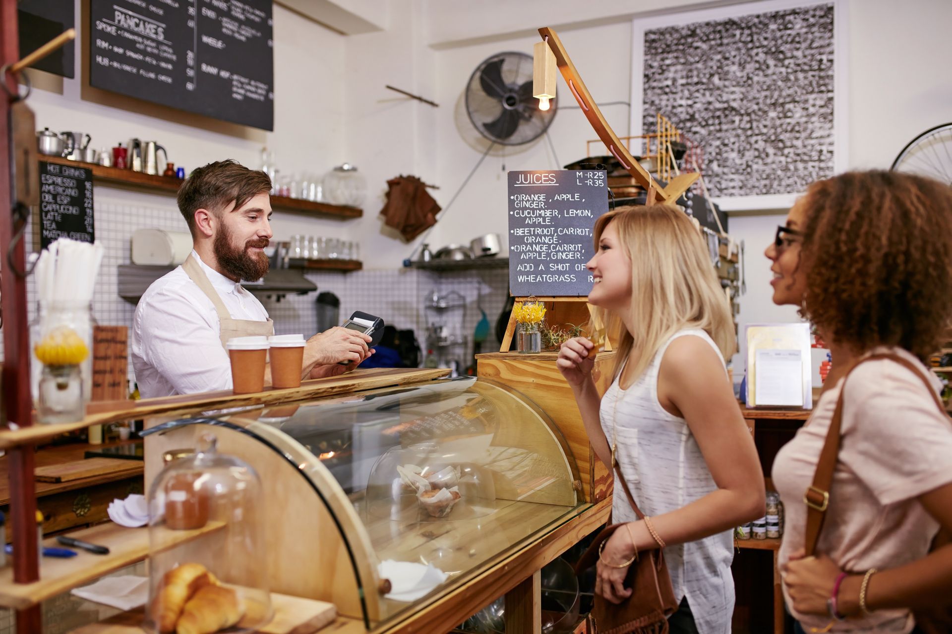 A barista taking an order from two customers at a cafe counter.