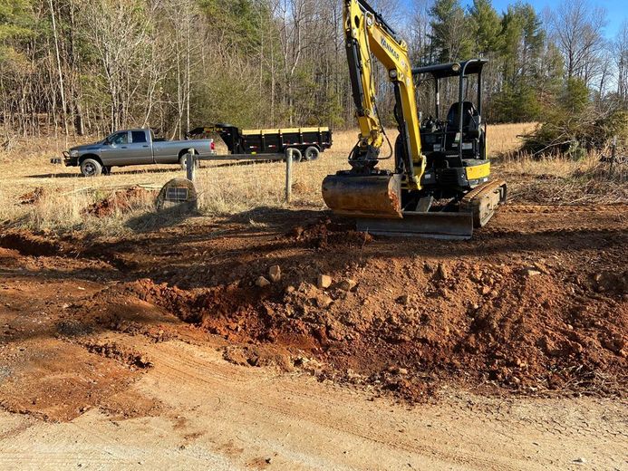 A yellow excavator is moving dirt in a field next to a truck.