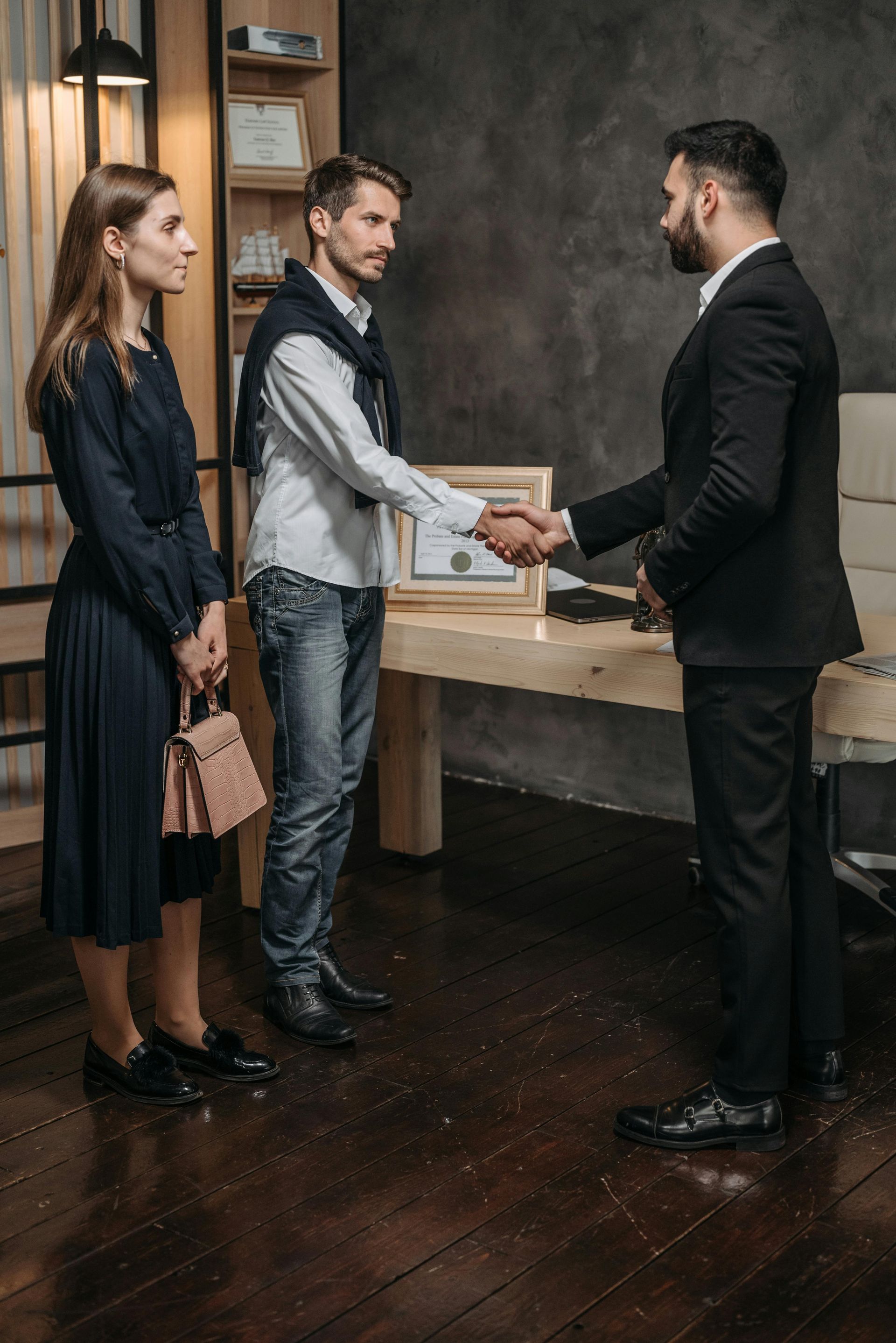 Couple shaking hands with a man in a suit at an office. A woman watches.