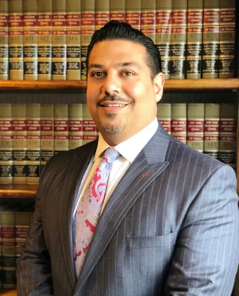 Man in suit, smiling, in front of law books.