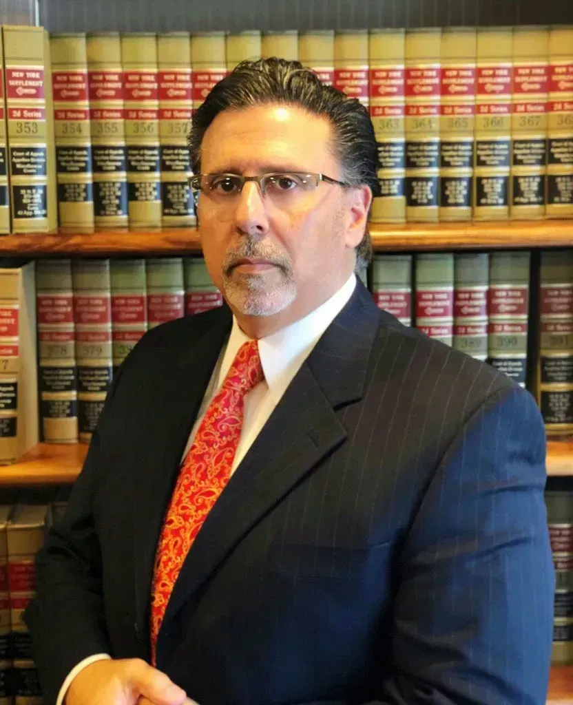 A man in a suit and tie stands in front of a bookshelf filled with books.