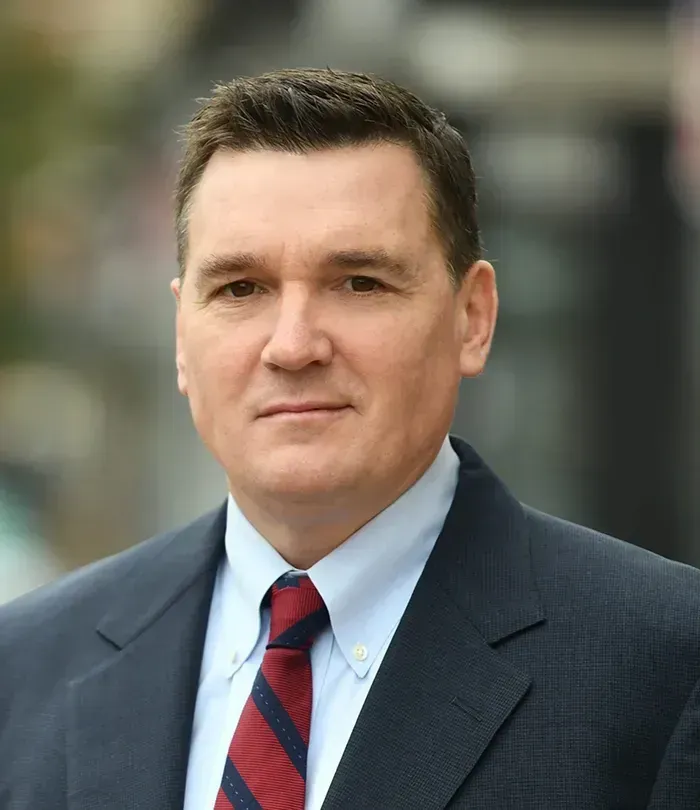 Man in suit and tie outdoors; looking at the camera with a neutral expression.