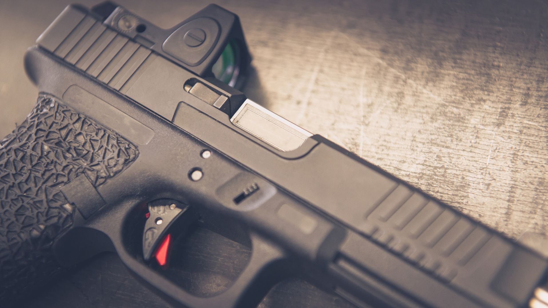 Black handgun with red trigger and red dot sight. Close-up on a textured surface.