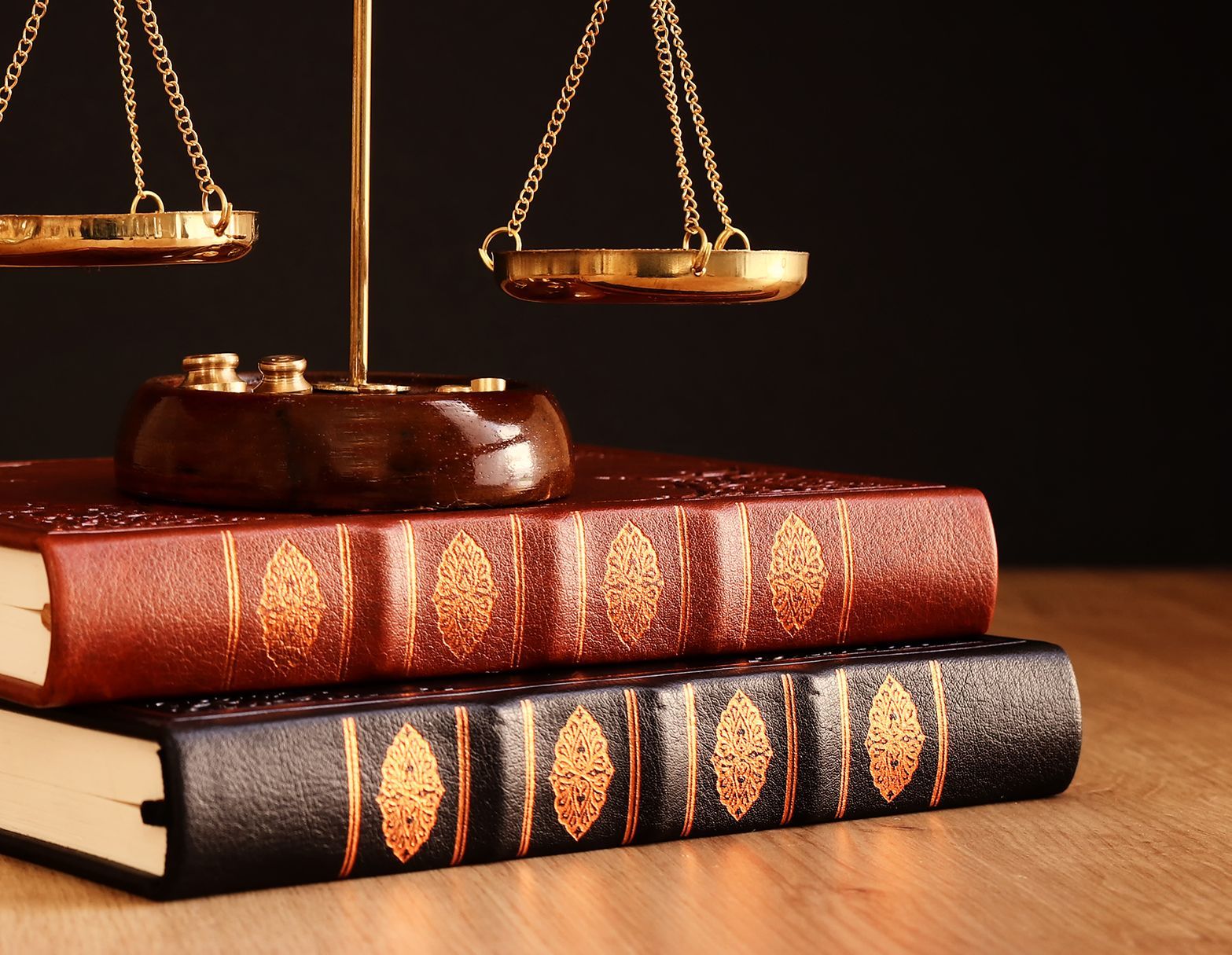 Scales of justice on top of two law books on a wooden surface against a dark background.