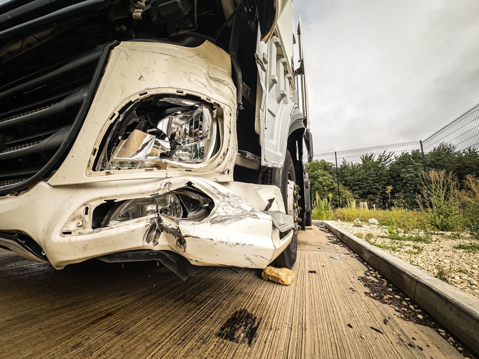 Damaged white truck on a roadside after a collision; the front is severely damaged.