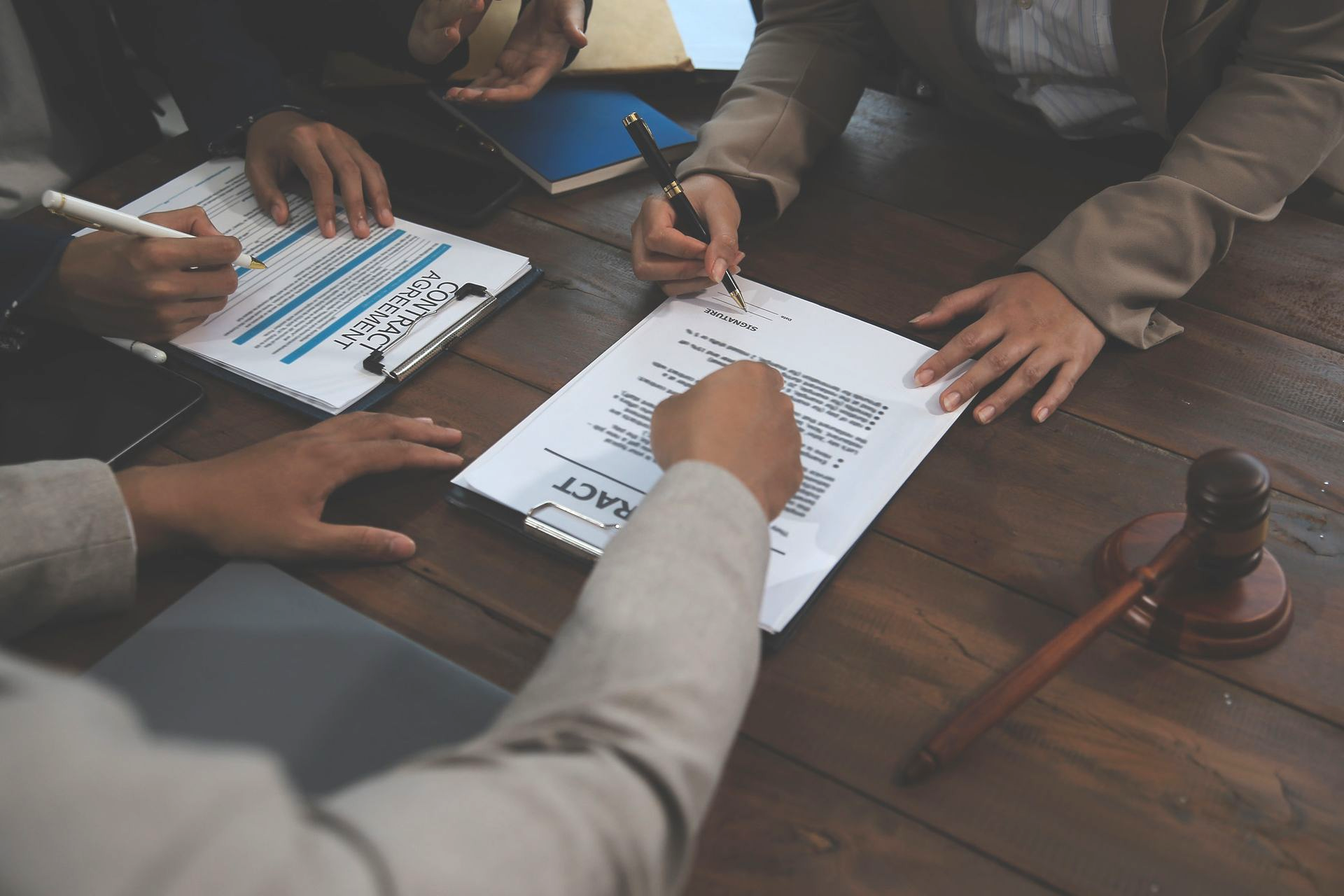 People signing documents at a wooden table; a gavel rests on the right.