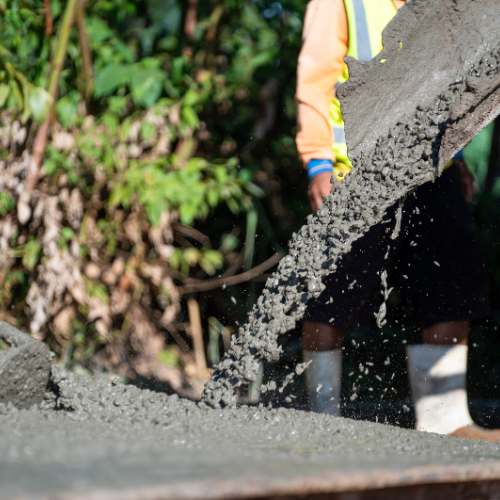 Concrete being poured by a construction worker wearing a safety vest.