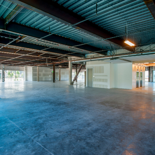 Empty commercial space with concrete floor and exposed ceiling, natural light streaming in.