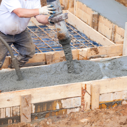 Man pouring concrete into wooden formwork on construction site.
