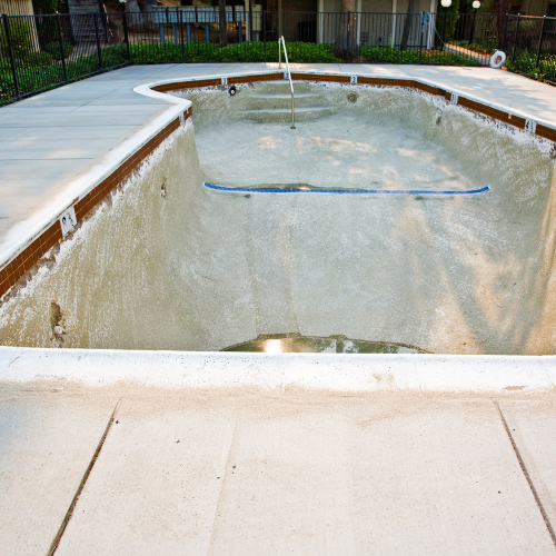 Empty swimming pool with concrete deck, brown trim, and a blue pool brush.