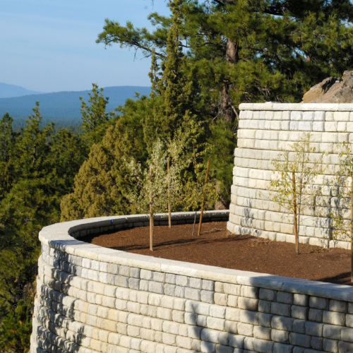 Stone retaining wall with small trees, overlooking mountains and trees.