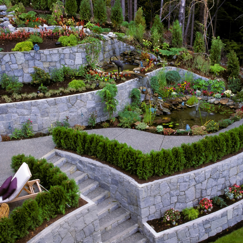 Multi-tiered garden with stone walls, steps, and a small pond with flowers.