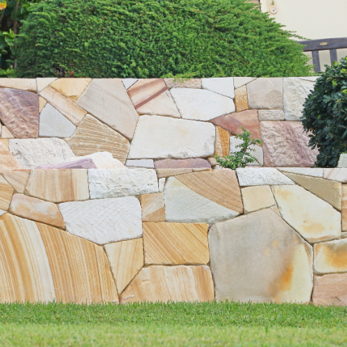 Stone retaining wall with various color sandstone, green grass, and bush.
