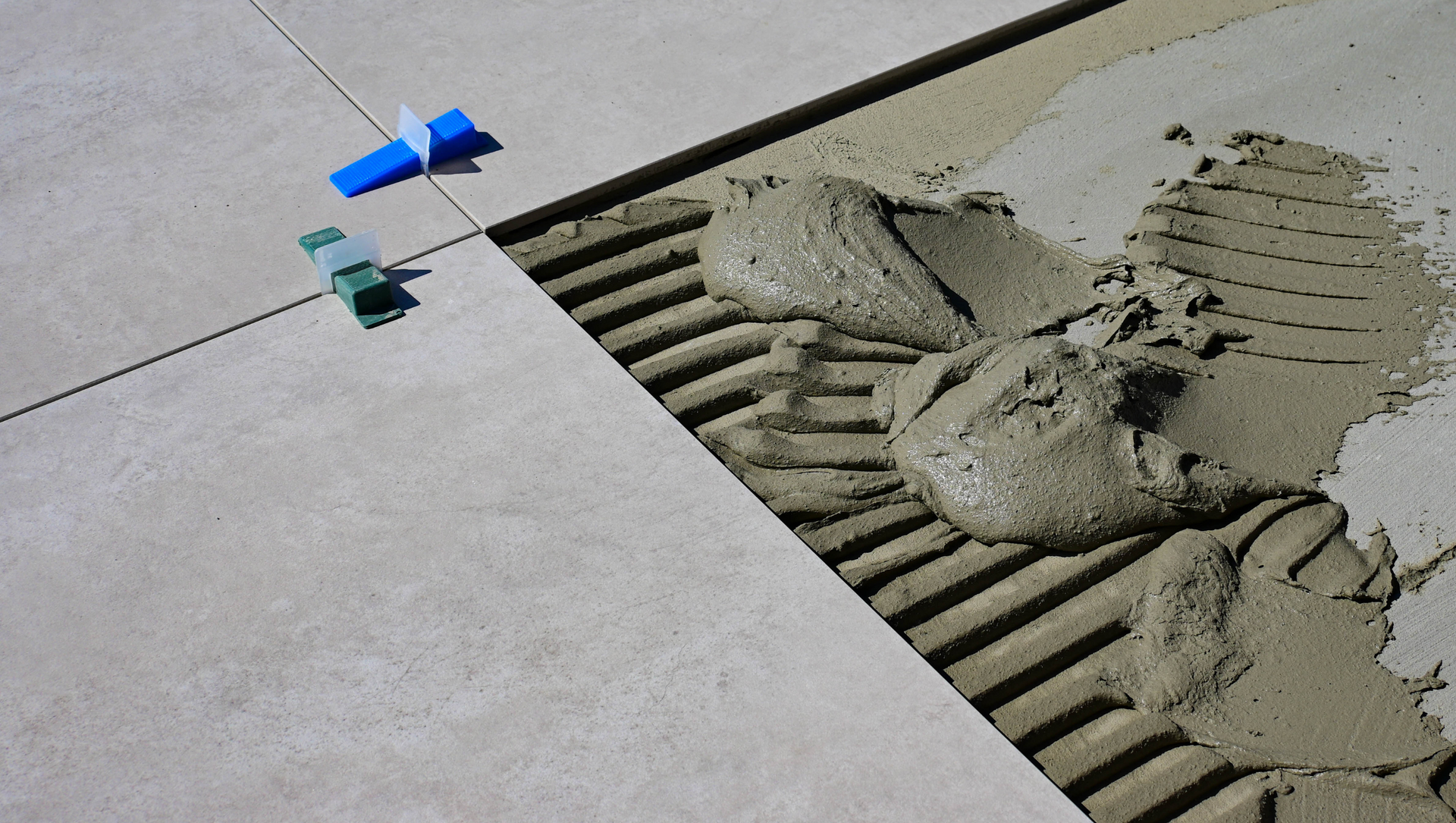 Tile being laid with notched trowel marks, mortar, and leveling clips; close-up view.