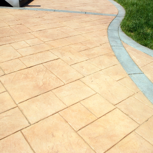 Tan stamped concrete pathway with a grey border, curving next to green grass.