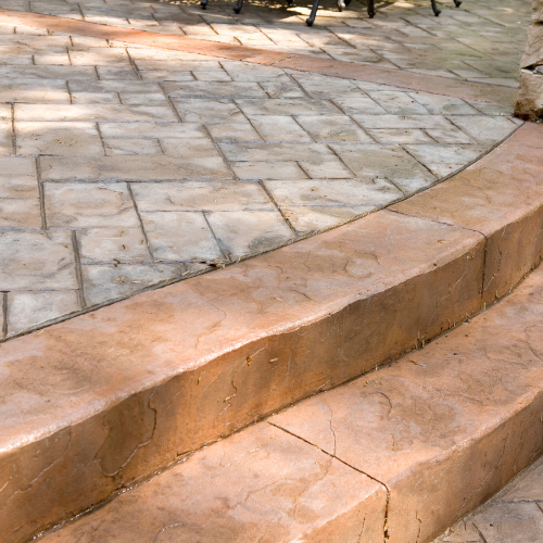 Concrete patio with two steps, featuring textured stonework in tan and brown hues.