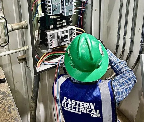 Electrician in green hard hat working on an electrical panel. Eastern Electrical vest.