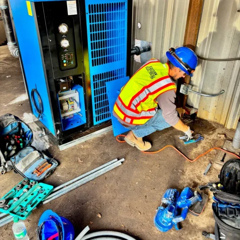 A worker in safety gear repairs electrical equipment in an industrial setting.
