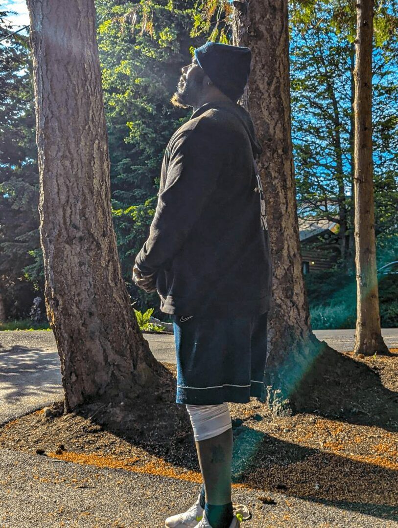 A man is standing next to a tree in the woods.