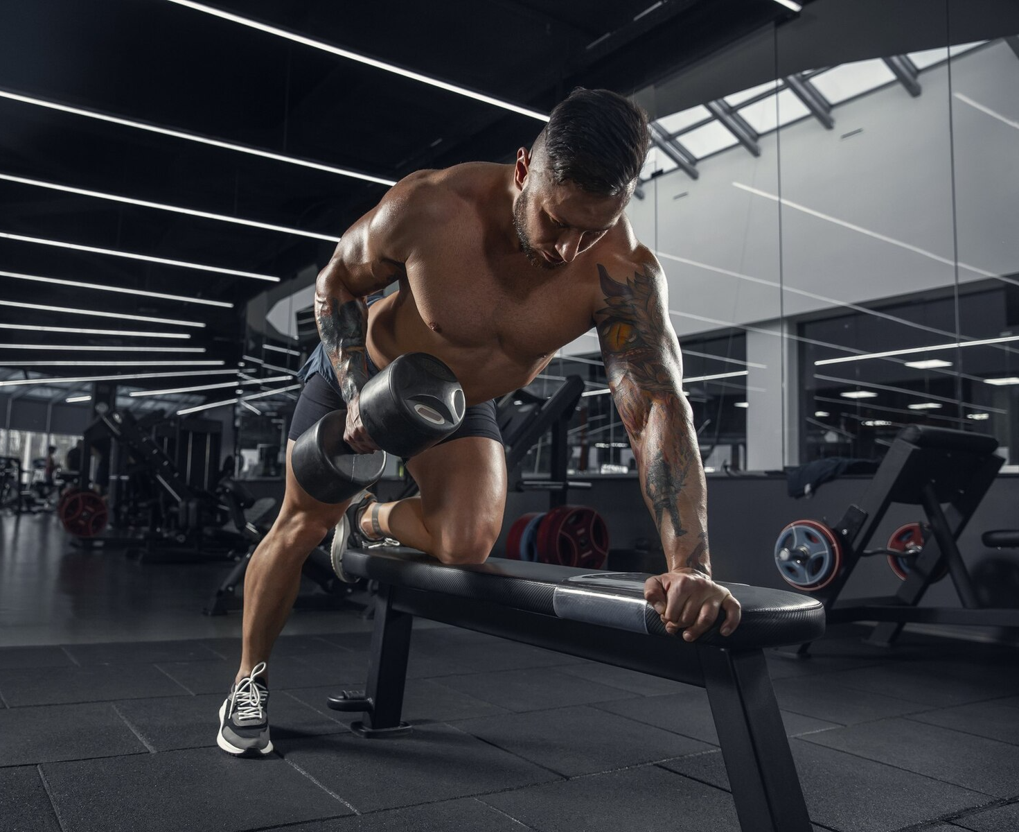 A shirtless man is lifting a dumbbell on a bench in a gym.