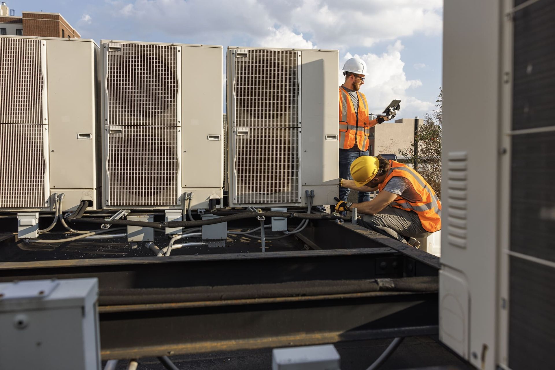 Workers wearing protective gear, performing commercial HVAC repair, inspecting AC on a rooftop.