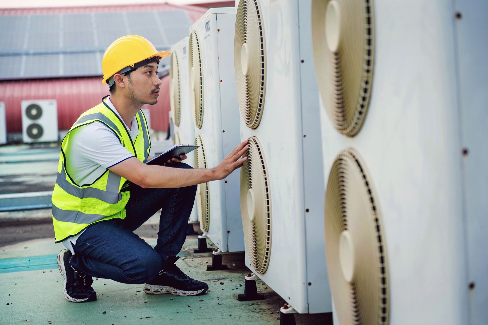 A man in a yellow vest checking an air conditioner. A man in a yellow vest checking an air conditioner.