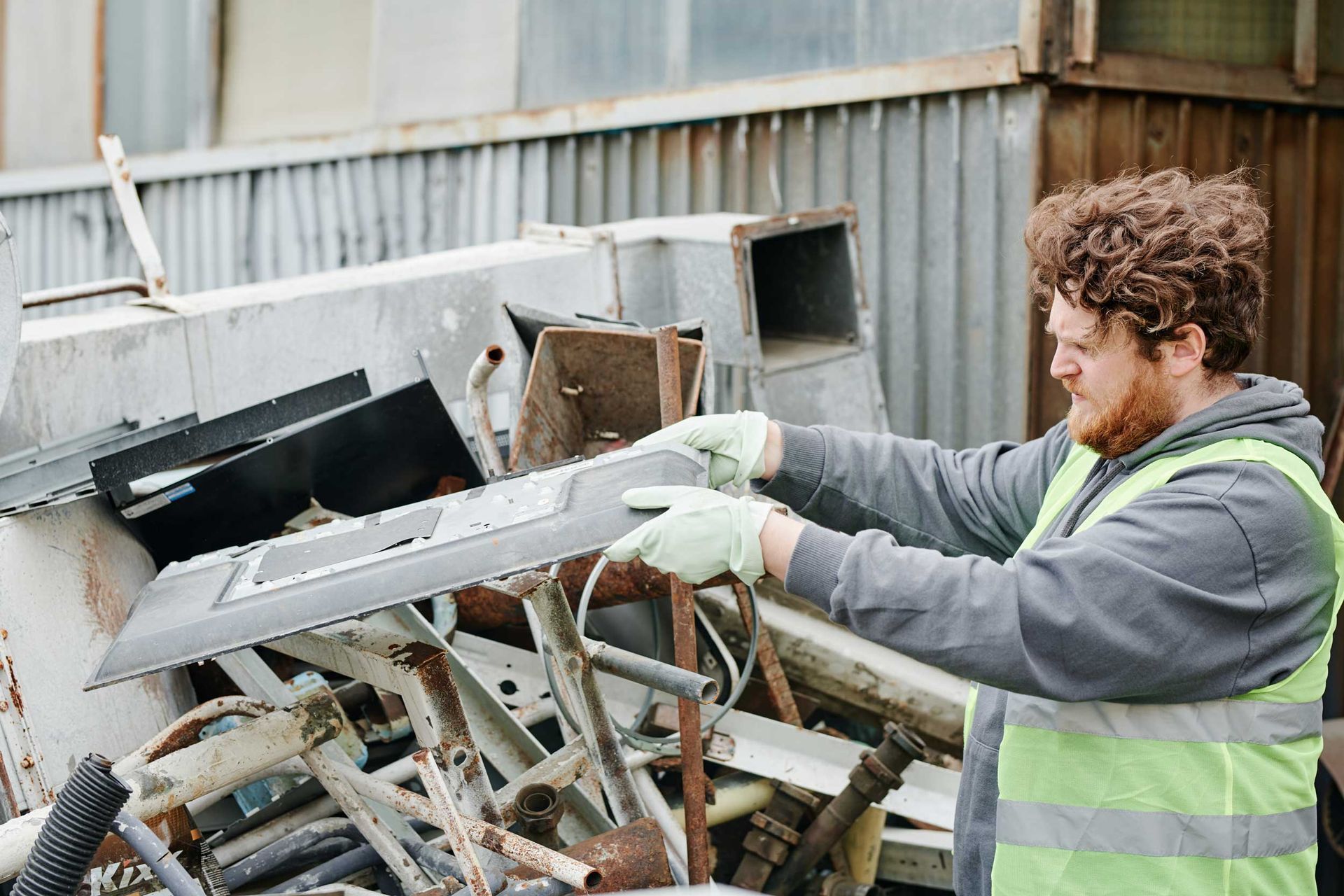 A worker is sorting collected scrap metals in a pile outdoors.