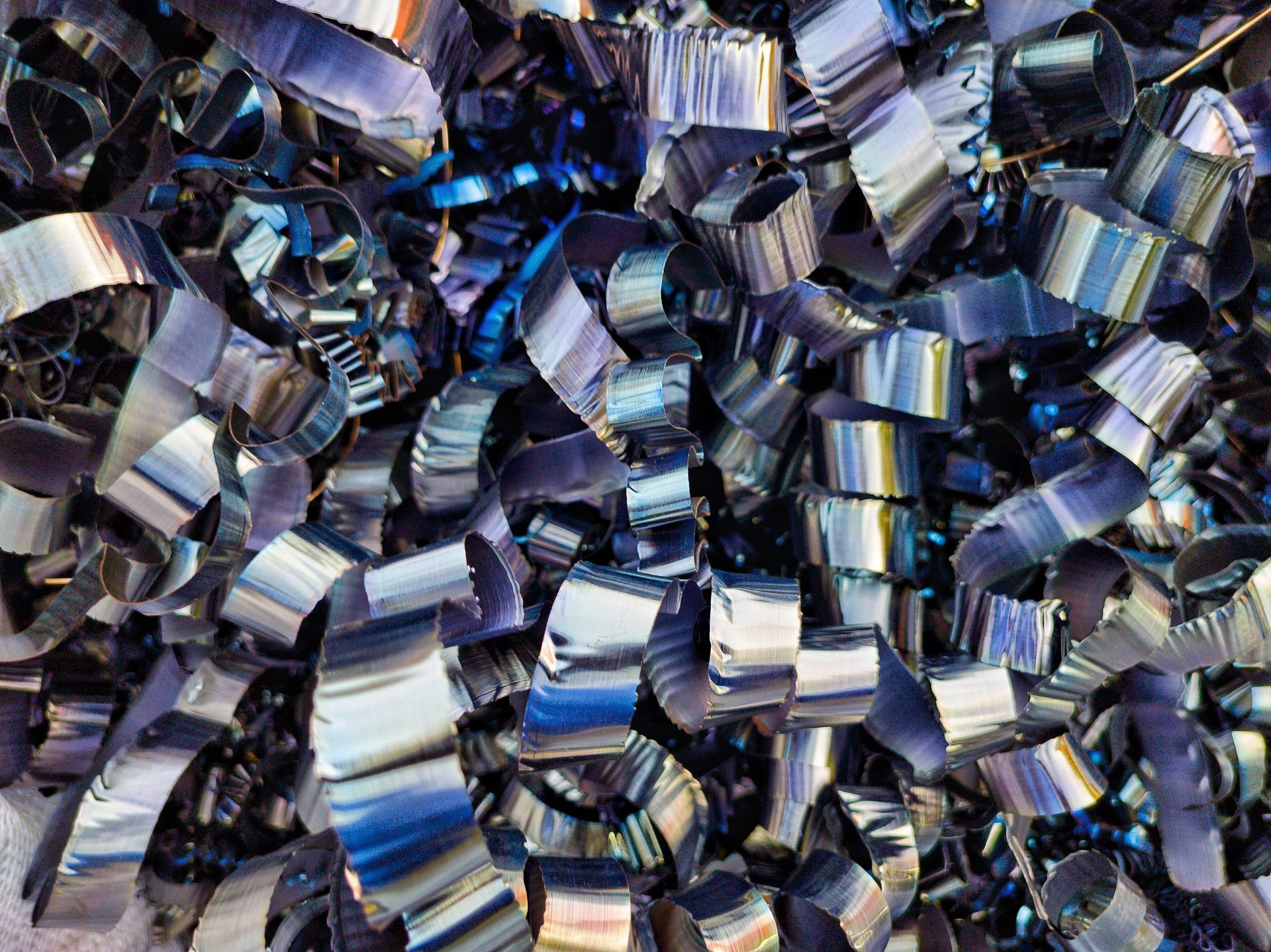 Shiny, curled metal shavings in varying shades of silver and blue, likely from a machining process.