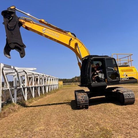 Yellow excavator with black tracks, equipped with a demolition grab, positioned