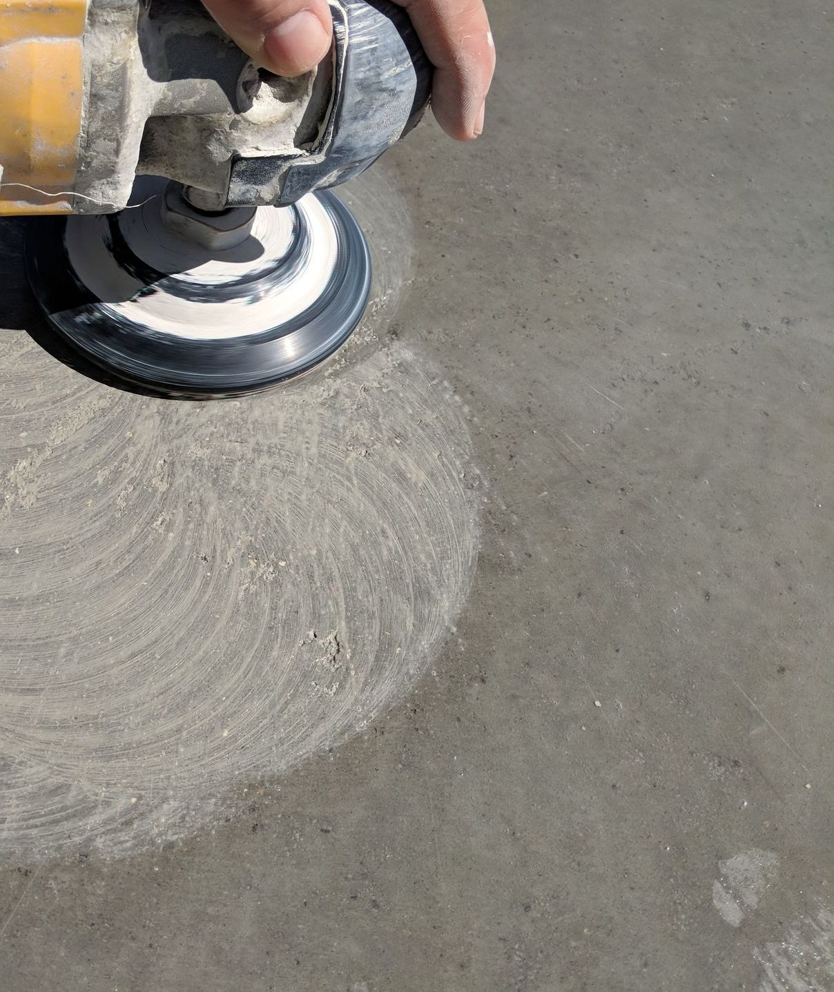 A person is sanding a concrete surface with a sander.
