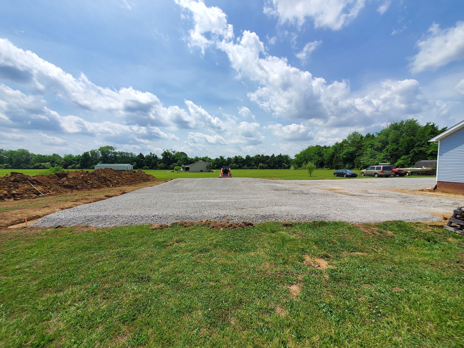 A gravel-filled rectangular area for a building foundation sits in a grassy yard under a blue, cloudy sky.