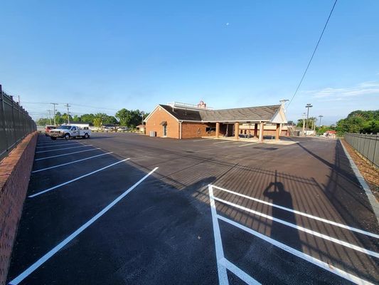 A paved parking lot with freshly painted white lines leads to a brick commercial building with a covered entrance.