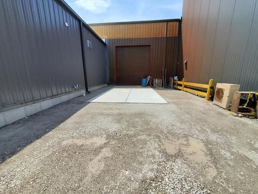 Concrete loading bay outside a warehouse with metal walls and a large, closed roll-up door.