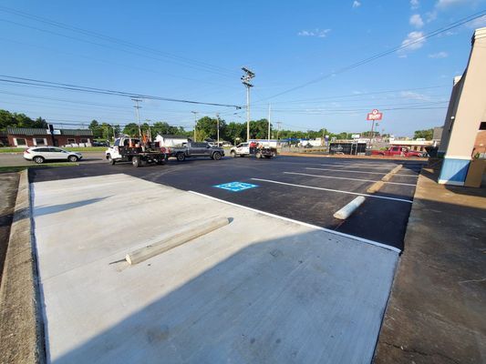 Newly paved parking lot featuring a concrete handicapped space with a blue symbol and marked asphalt parking stalls.