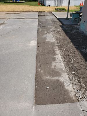 A concrete walkway with a long, rectangular patch of dark, freshly filled soil or gravel running down the middle.