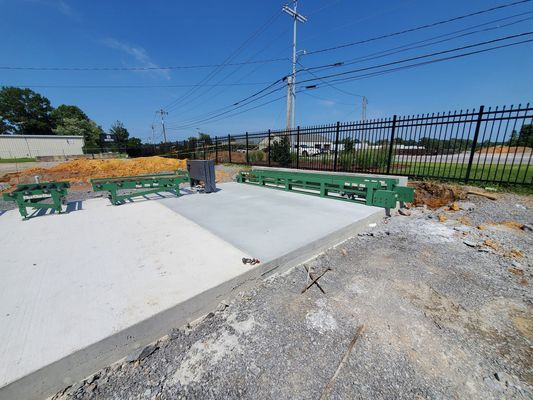 Green metal guardrails installed on a concrete foundation pad next to a black fence under a clear blue sky.