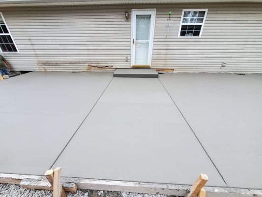 A freshly poured grey concrete patio with a step leading to a house door, framed by wooden construction forms.