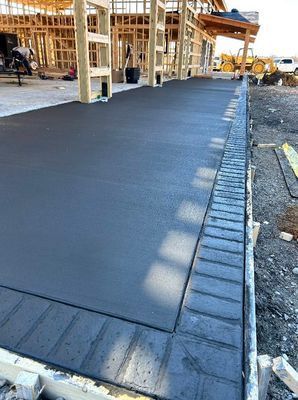 A freshly poured concrete patio with a dark, stamped brick-patterned border at a construction site.