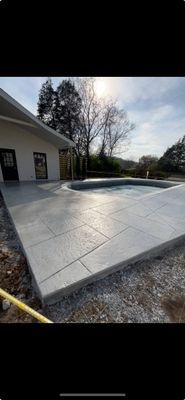 A light-colored house with a stamped concrete patio and an adjacent swimming pool under a bright sky.