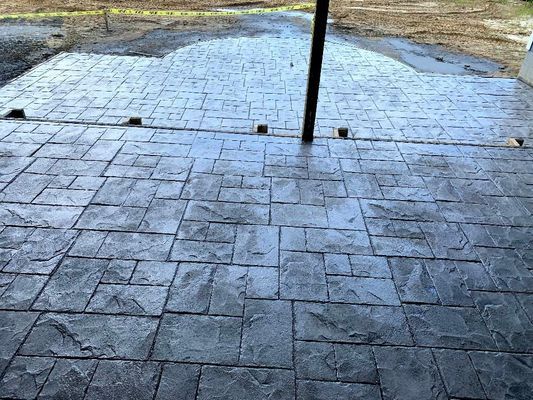 Gray stamped concrete patio with a rectangular stone pattern, extending from a dark support post toward an outdoor area.